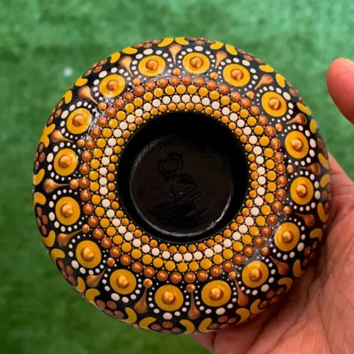 Round tea light holder covered in orange and gold dot-painted patterns
